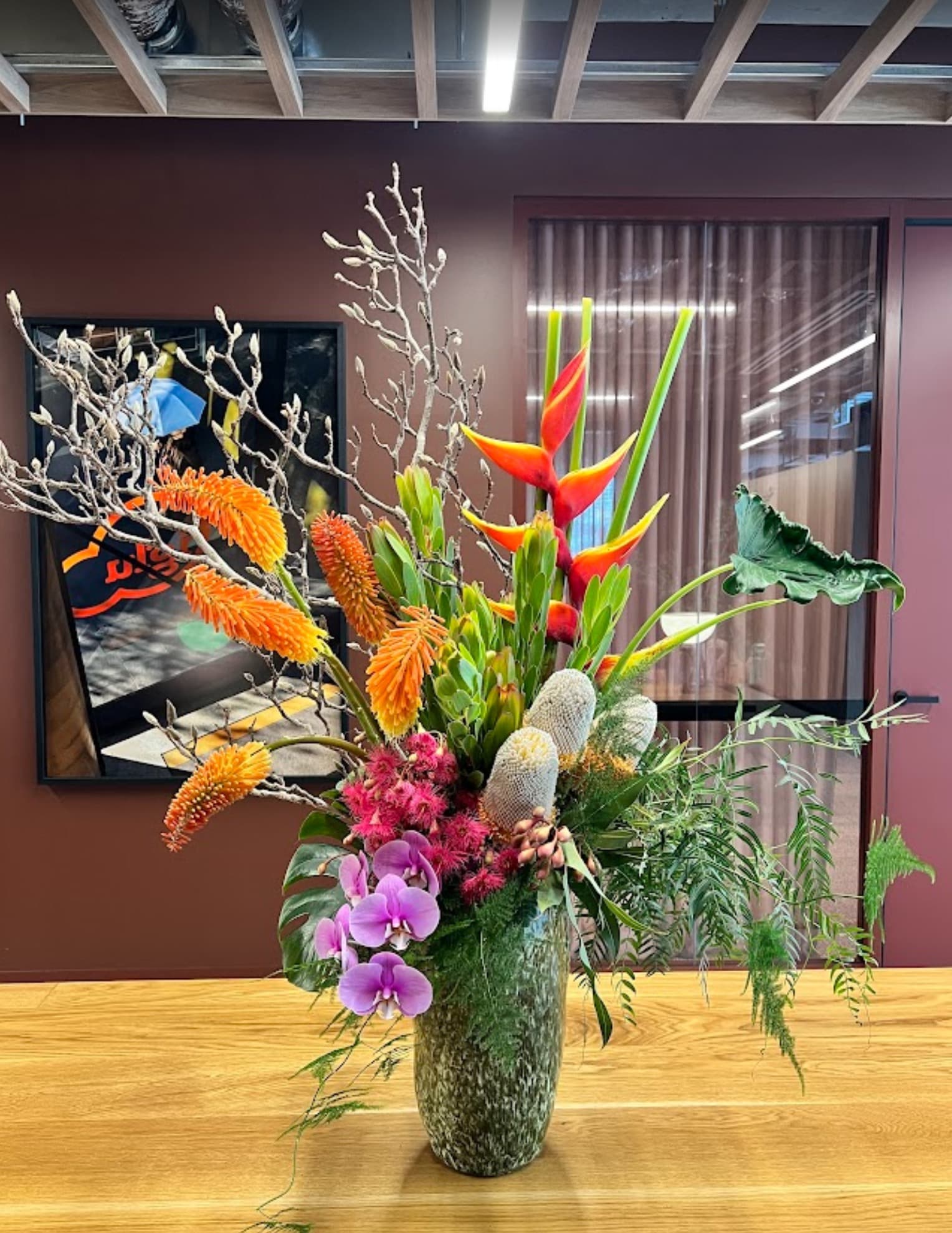 A tall arrangement of heliconia, orchids and banksia in a stone vase