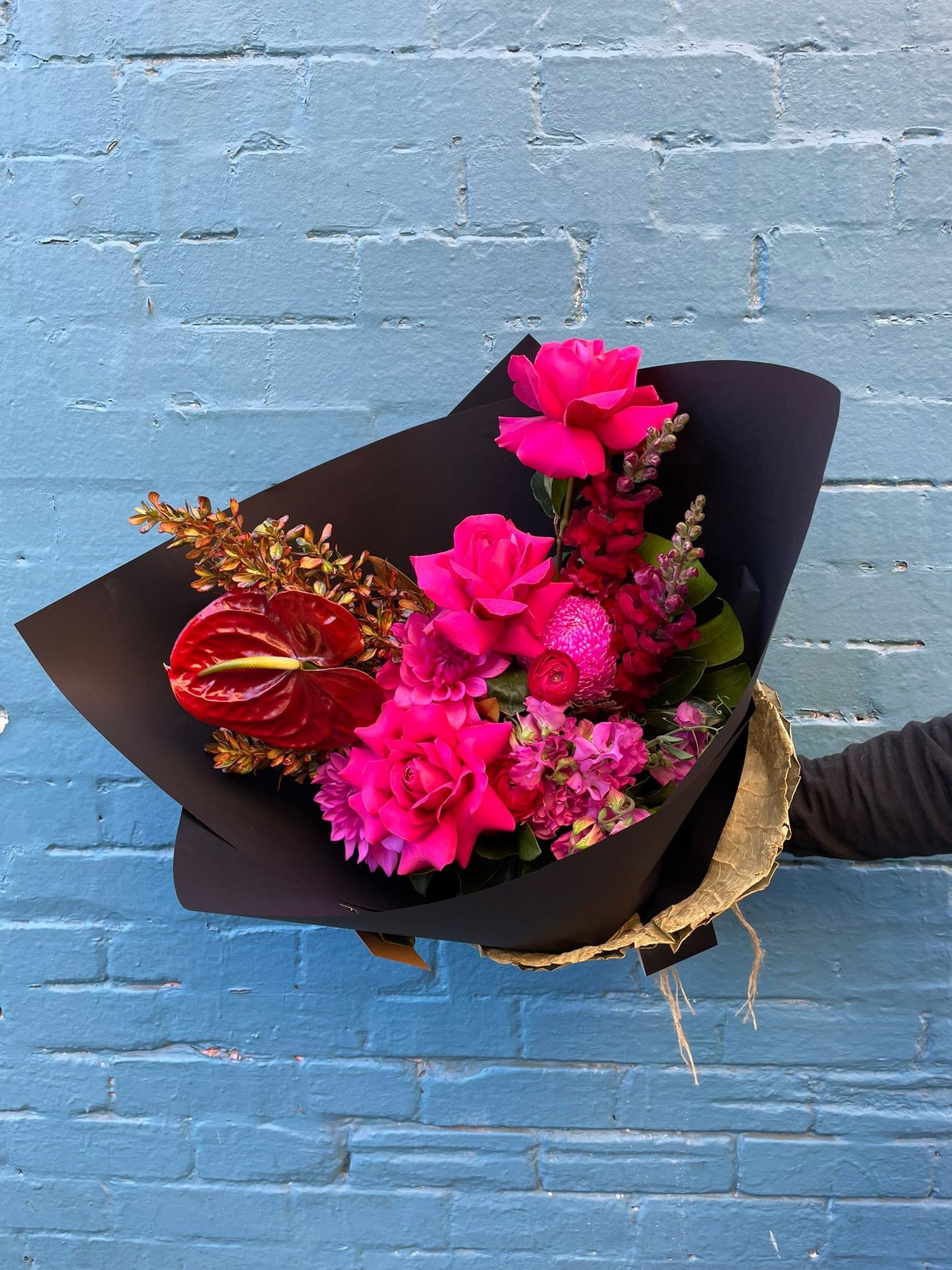 A pink and red hand-tied bouquet against a blue wall