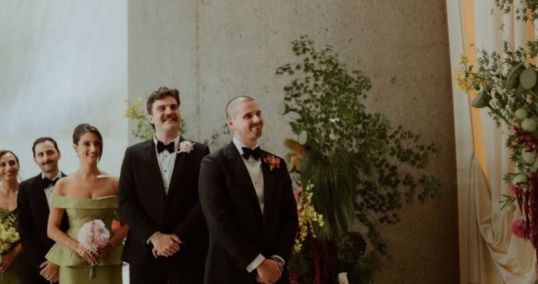 A wedding party beside a green and floral ceremony installation